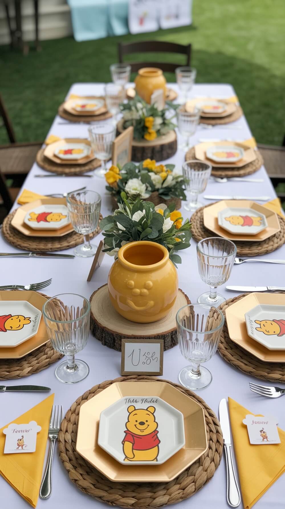 Winnie The Pooh themed baby shower table setting with plates featuring Pooh Bear, a hunny pot centerpiece, and floral decorations.